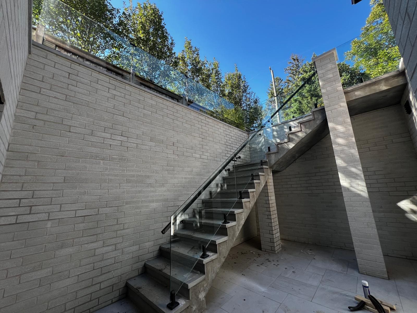 Glass-guarded exterior stair climbing a brick retaining wall, installed by the Reis Glass crew