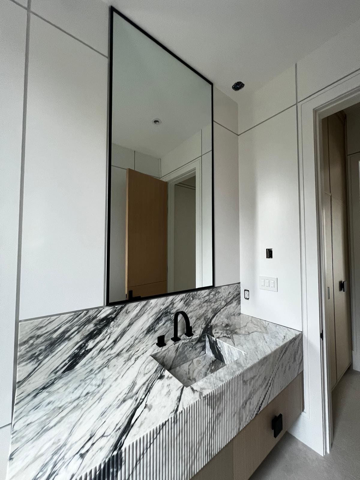 Tall black-framed mirror over a marble vanity