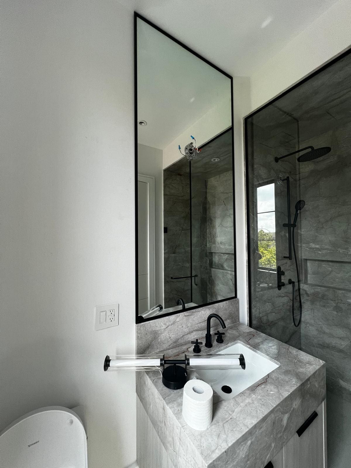 Black-framed glass shower beside a marble vanity