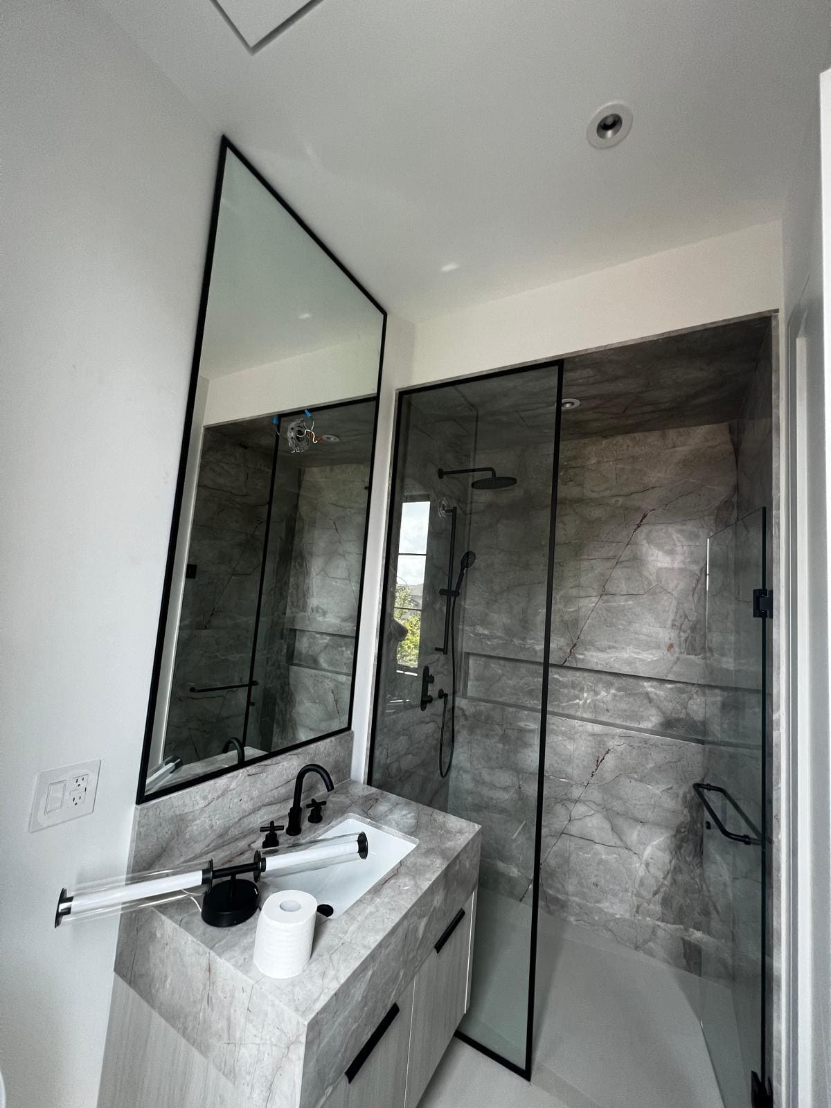 Black-framed glass shower beside a marble vanity