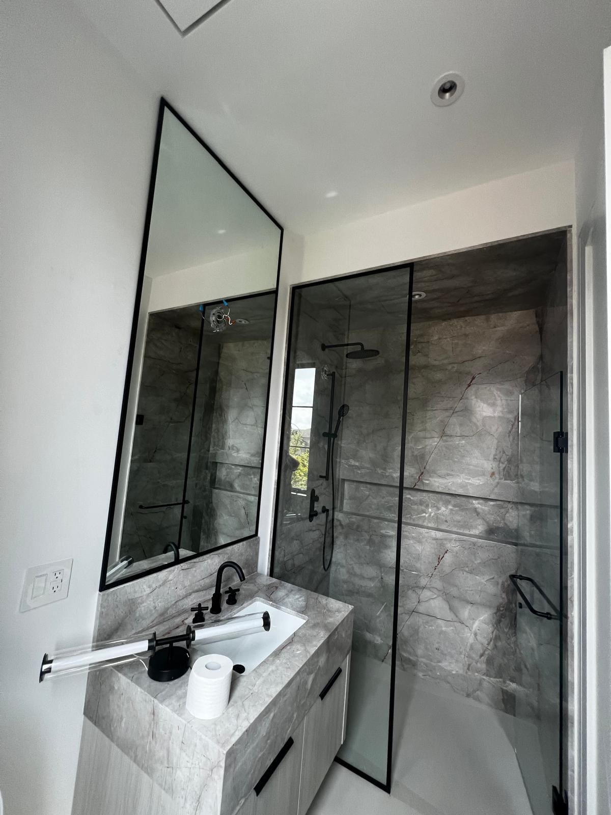 Black-framed glass shower beside a marble vanity