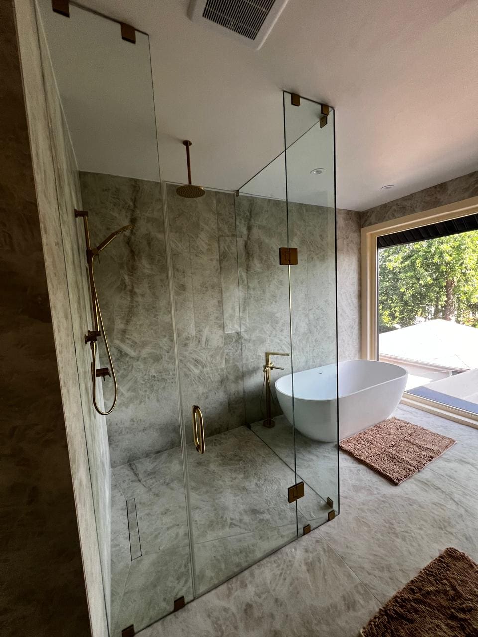 Frameless shower with brushed gold hardware in a stone ensuite