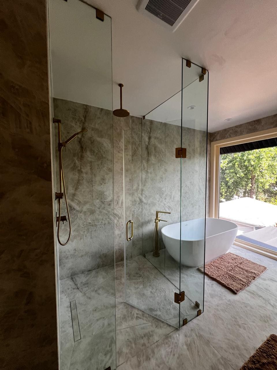 Frameless shower with brushed gold hardware in a stone ensuite