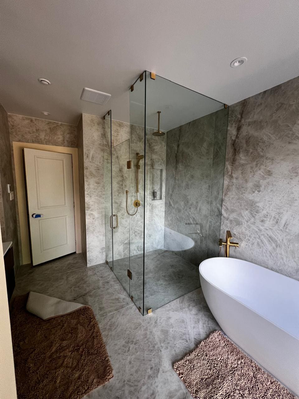 Frameless shower with brushed gold hardware in a stone ensuite