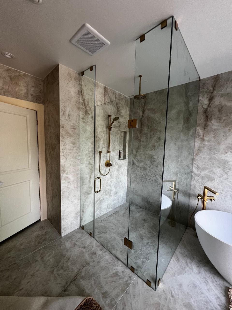 Frameless shower with brushed gold hardware in a stone ensuite