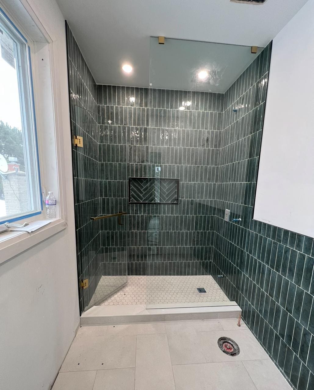 Frameless screen with gold hinges on a green-tile shower