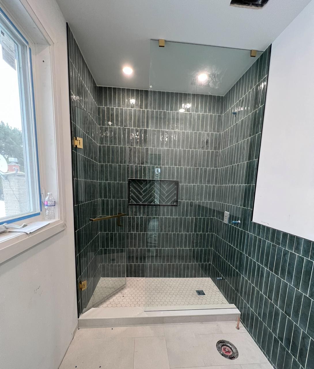 Frameless screen with gold hinges on a green-tile shower