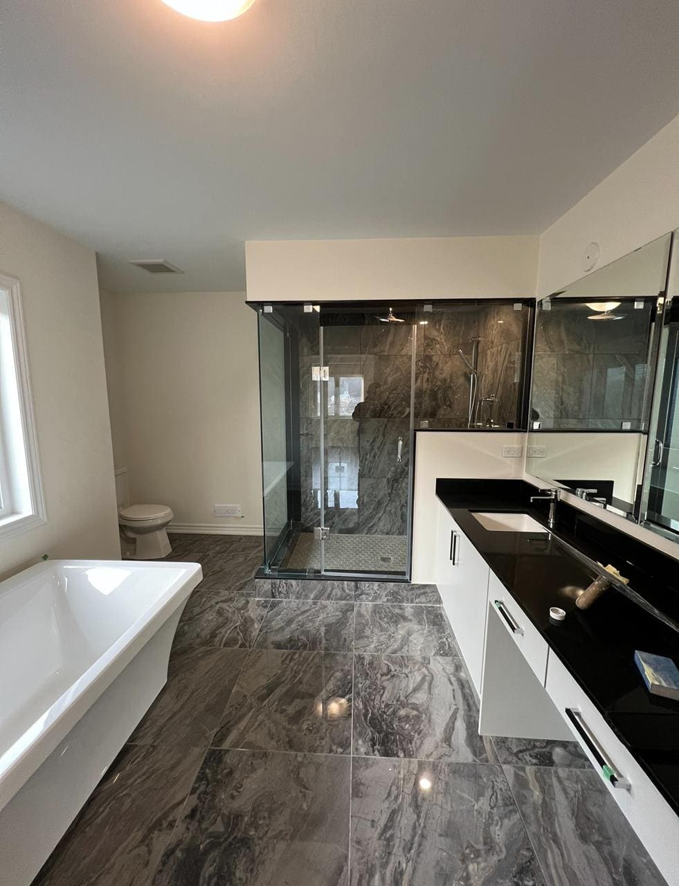 Floor-to-ceiling glass enclosure in a grey marble ensuite