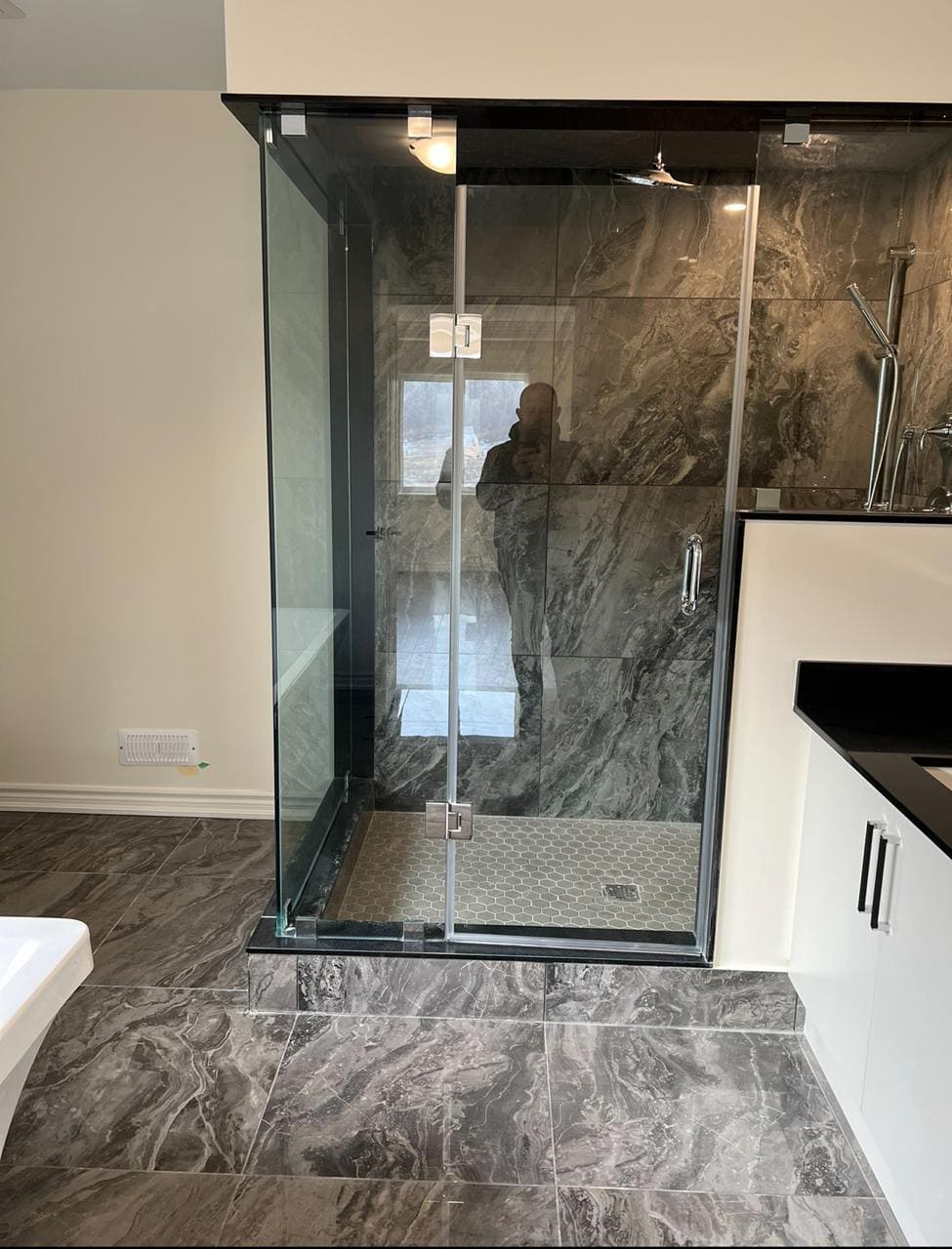 Floor-to-ceiling glass enclosure in a grey marble ensuite